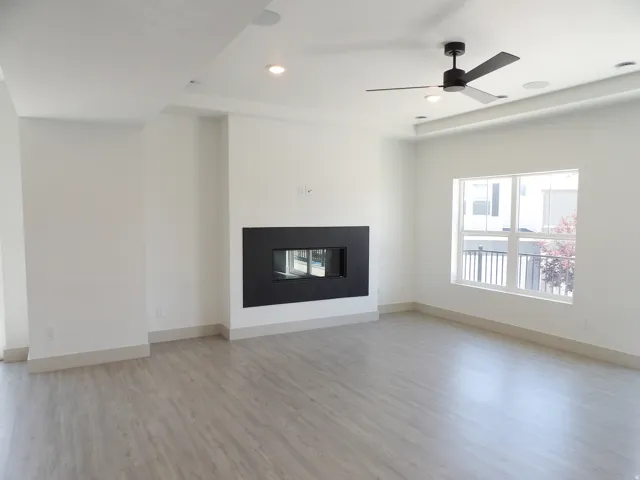 Spacious living area featuring a modern fireplace, wood-finish flooring, a contemporary ceiling fan, recessed lighting, and a large window
