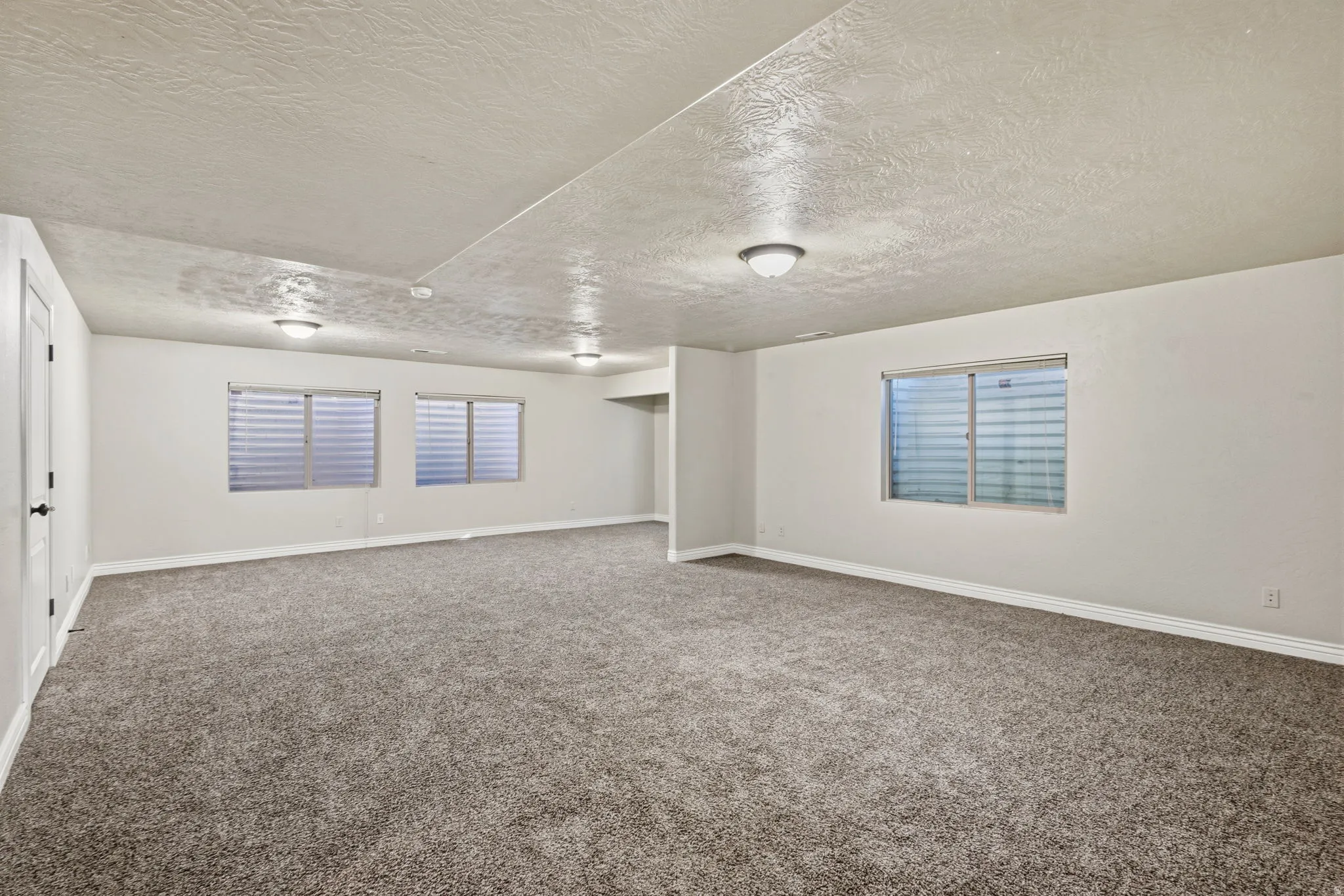 Expansive room featuring plush carpeting, multiple windows with horizontal blinds, and recessed lighting fixtures