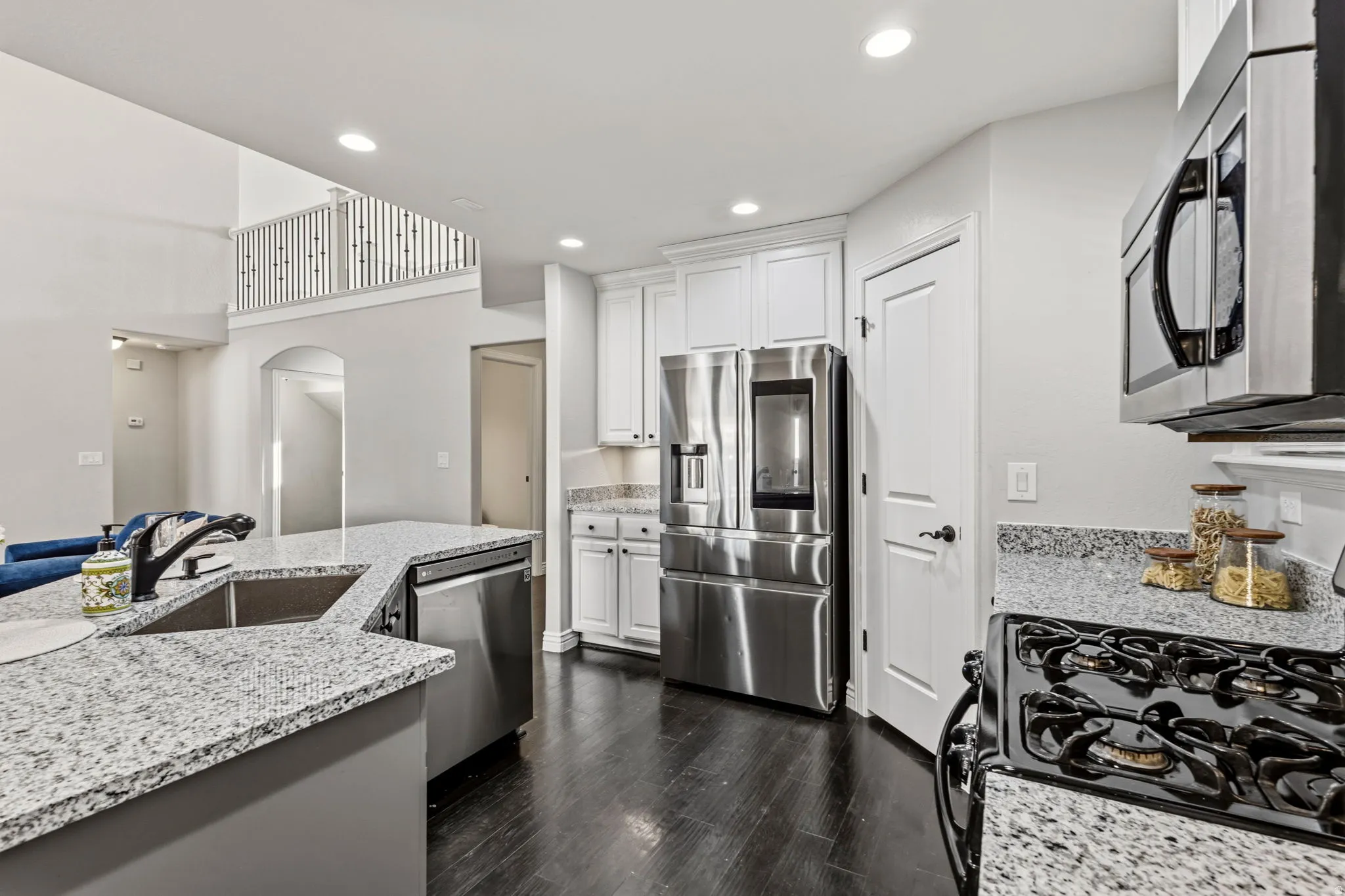 Kitchen featuring stainless steel appliances, granite countertops, white cabinetry, and wood-finish flooring