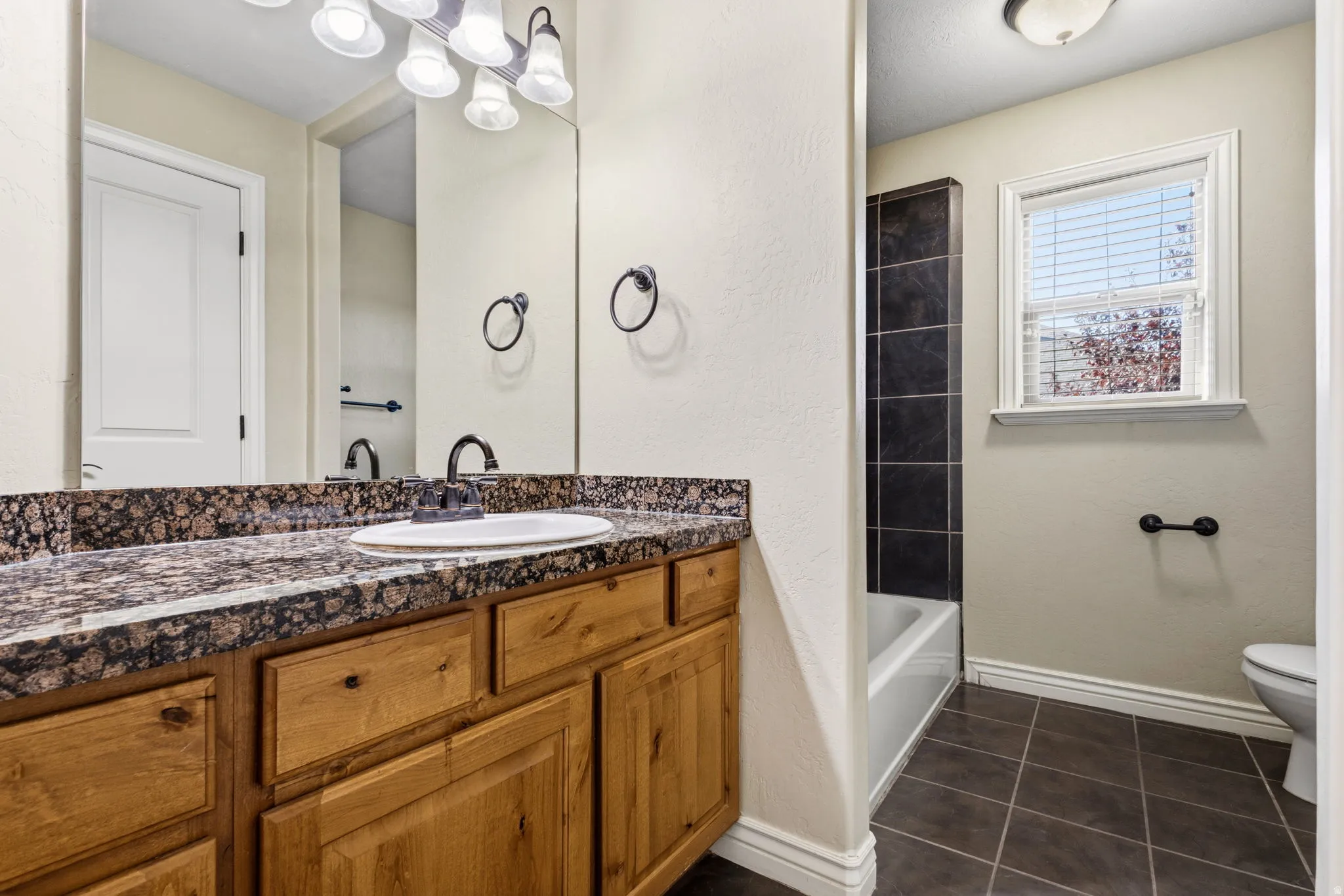 Bathroom vanity with a dark granite-style countertop and wood-finish cabinetry