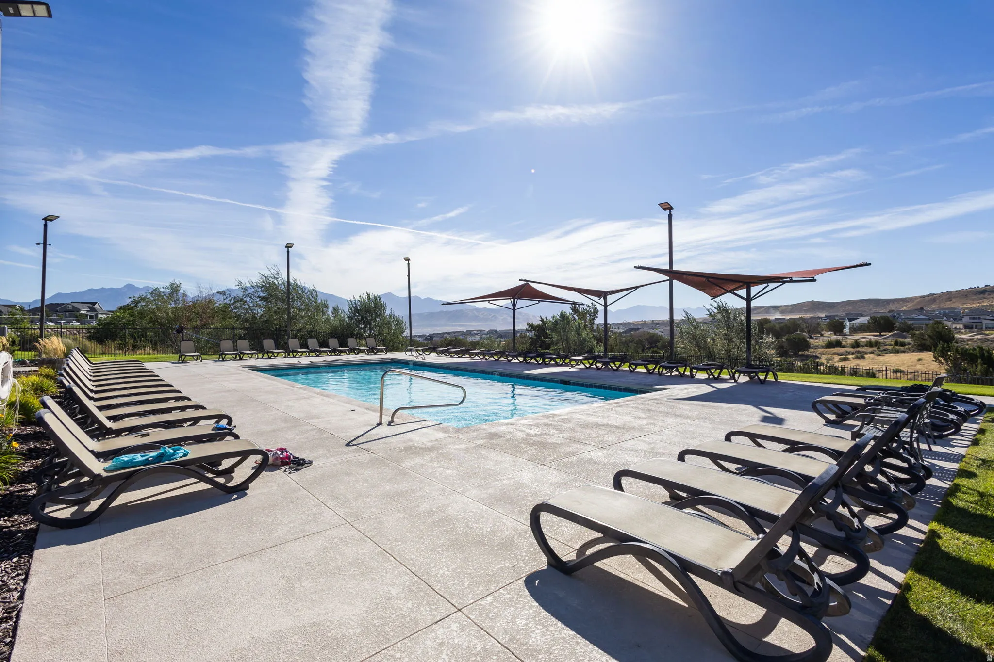 Outdoor swimming pool with concrete decking, sun loungers, and shade structures
