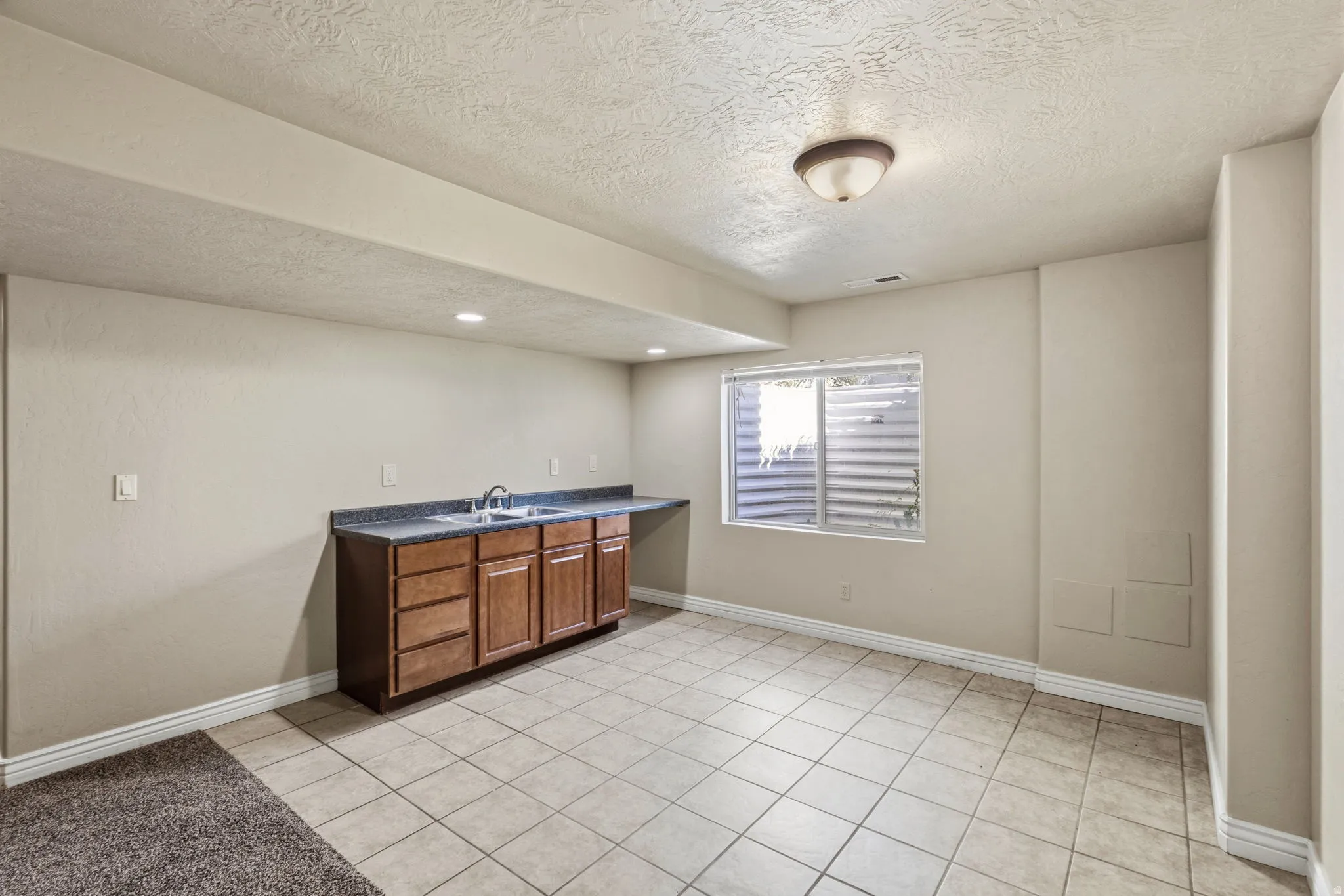 Built-in cabinetry with a dual basin sink, dark countertop, and tiled flooring