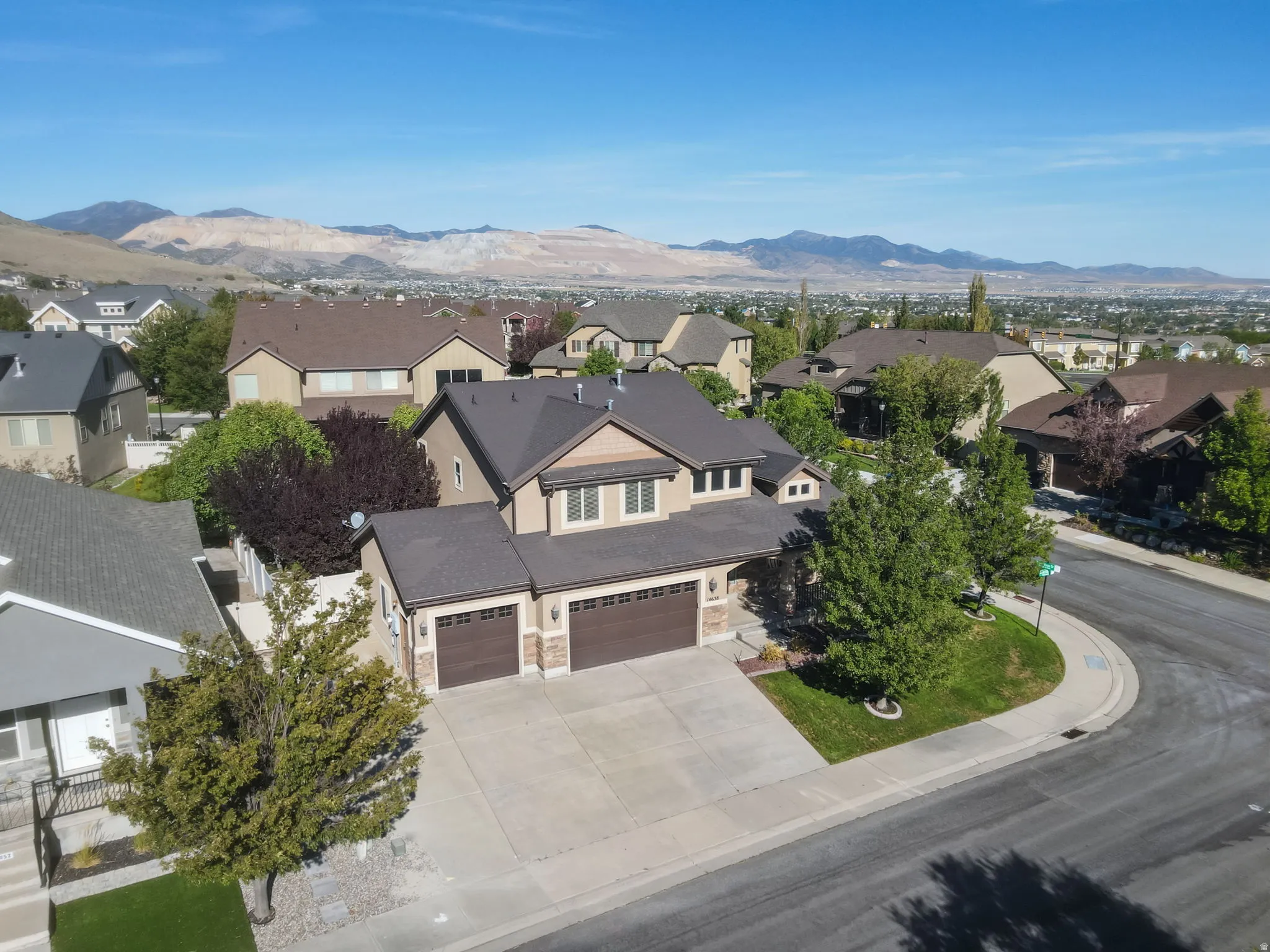 Multi-level residence featuring a dark shingle roof, light-toned stucco exterior, and a three-car garage