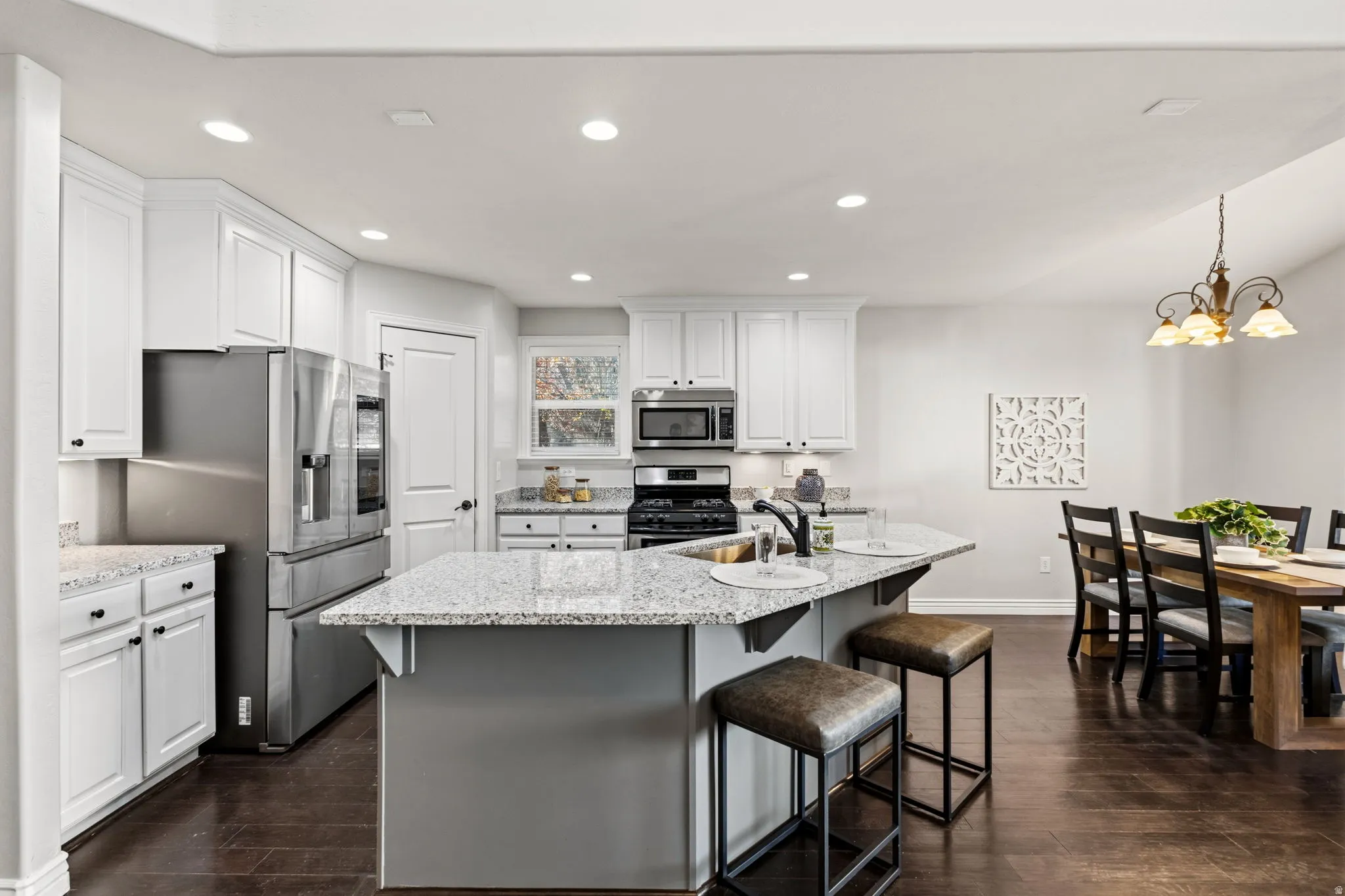 Kitchen featuring white cabinetry, stainless steel appliances, speckled stone countertops, and a central island with an undermount sink
