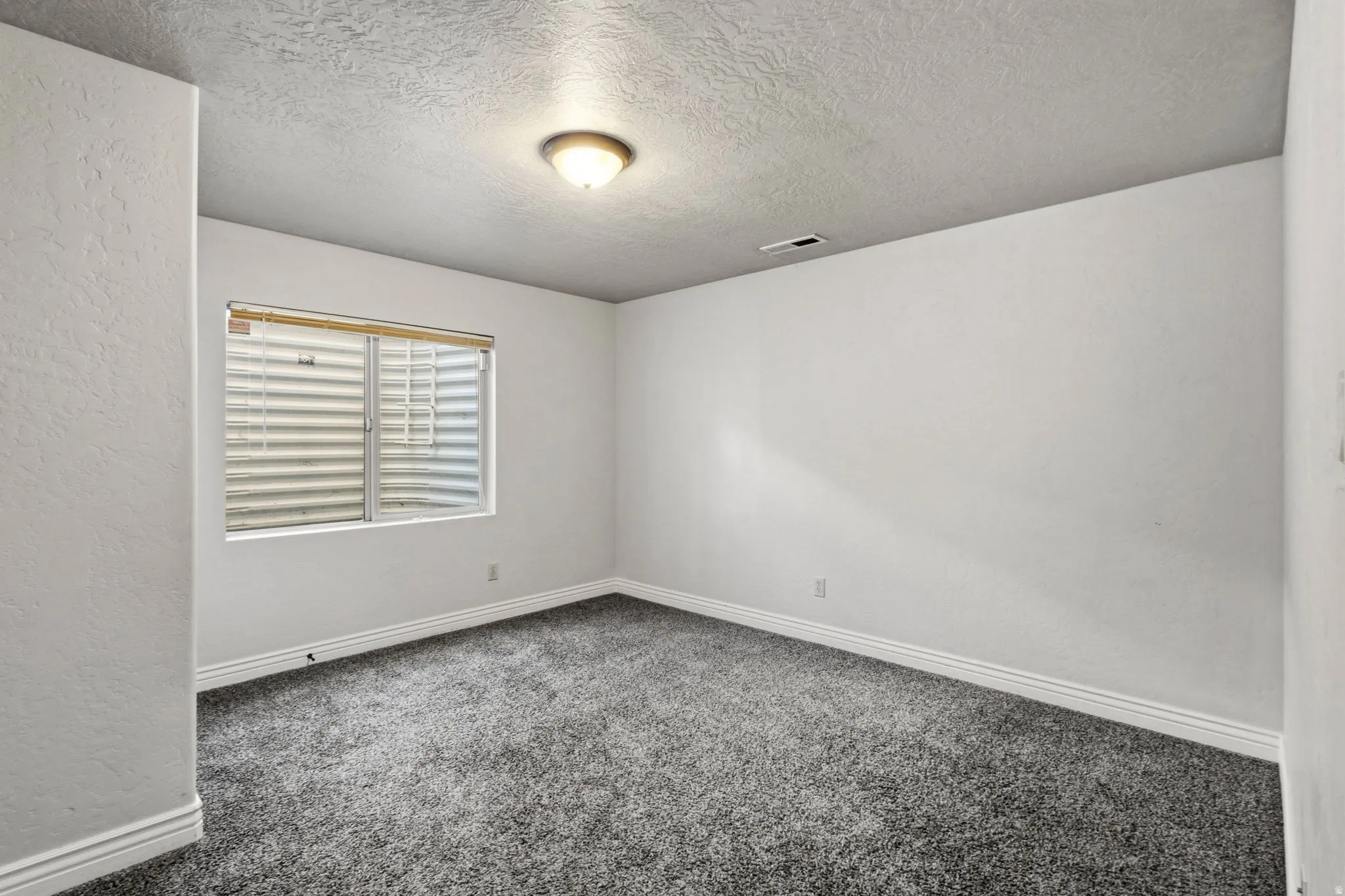 Textured walls with a neutral paint finish, grey carpet flooring, recessed window with blinds, and flush mount ceiling light