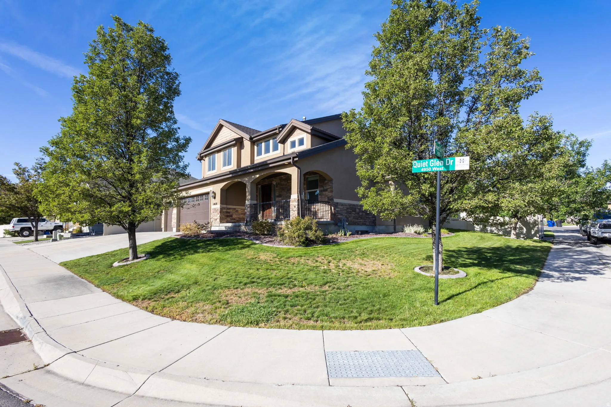 Corner lot with mature trees, a two-car garage, stone façade accents, and a covered front entry