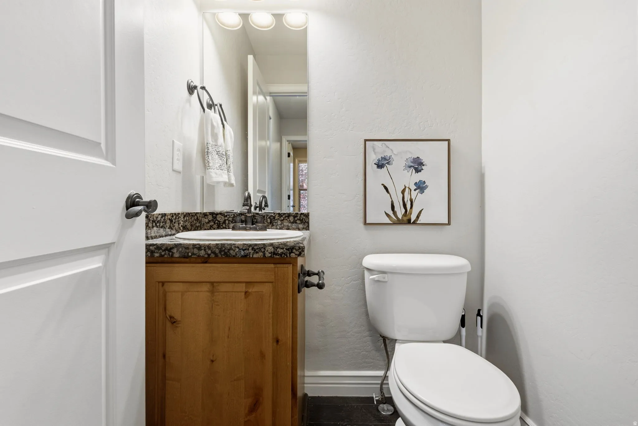 Wood-finish vanity with a surface-mounted sink, speckled stone countertop, and an integrated mirror with overhead lighting