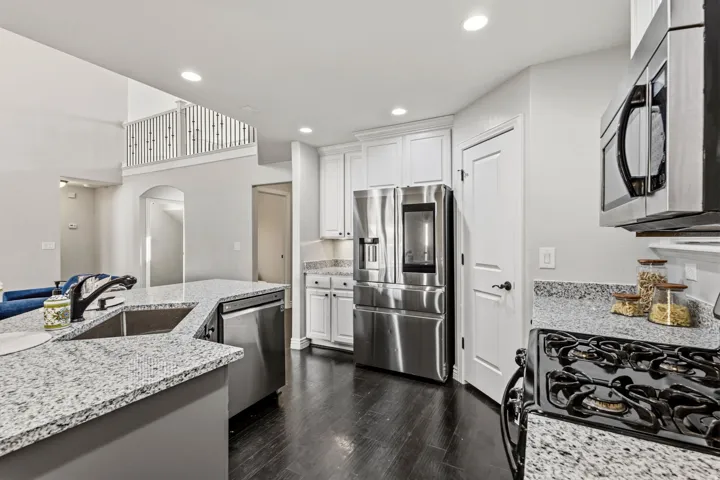 Kitchen featuring stainless steel appliances, granite countertops, white cabinetry, and wood-finish flooring