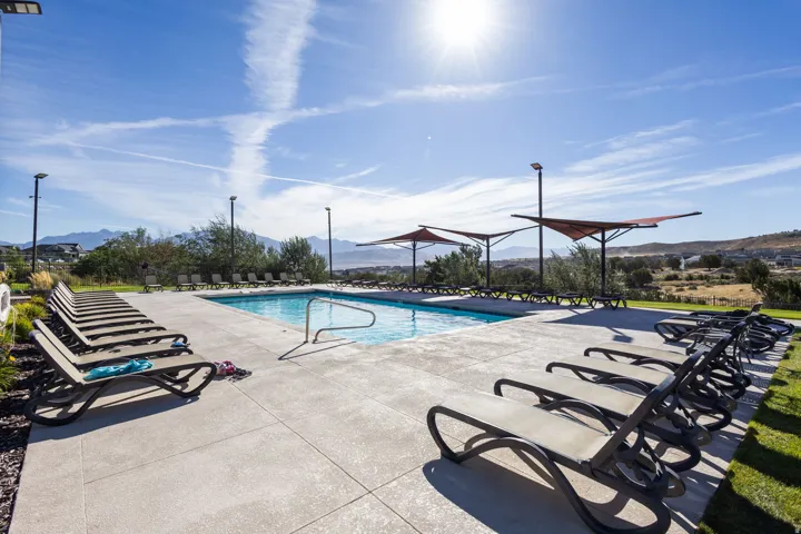 Outdoor swimming pool with concrete decking, sun loungers, and shade structures