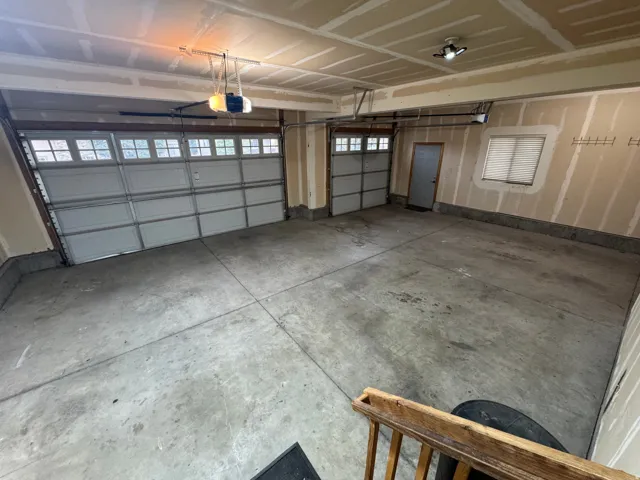 Two overhead garage doors with window inserts, concrete flooring, and an interior access door