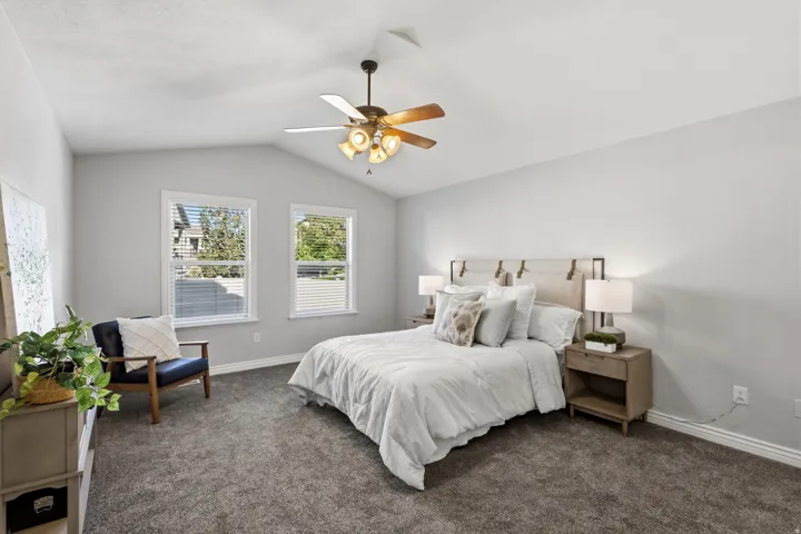 Vaulted ceiling featuring a ceiling fan, two double-hung windows, and wall-to-wall carpeting