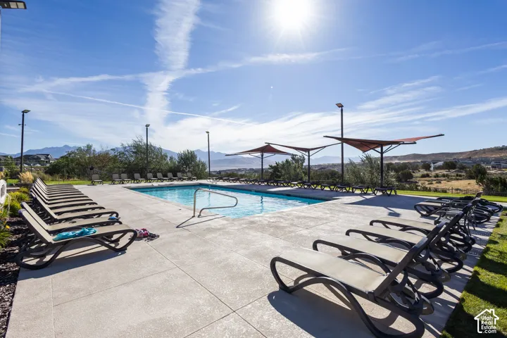 Outdoor swimming pool with concrete decking, sun loungers, and shade structures