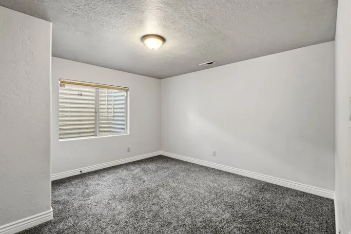 Textured walls with a neutral paint finish, grey carpet flooring, recessed window with blinds, and flush mount ceiling light