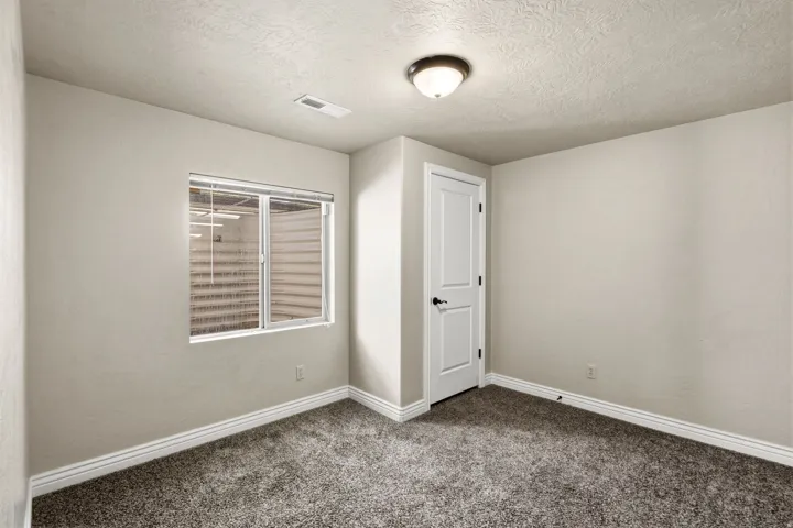 Neutral wall paint, textured ceiling, window with blinds, paneled door with dark hardware, and carpet flooring