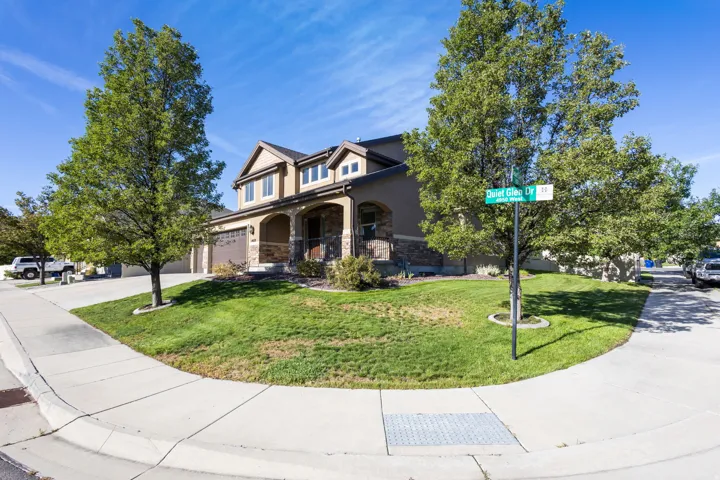 Corner lot with mature trees, a two-car garage, stone façade accents, and a covered front entry