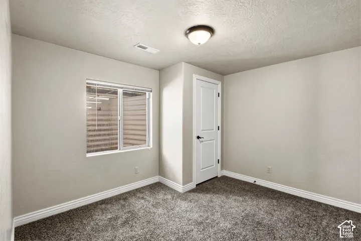 Neutral wall paint, textured ceiling, window with blinds, paneled door with dark hardware, and carpet flooring