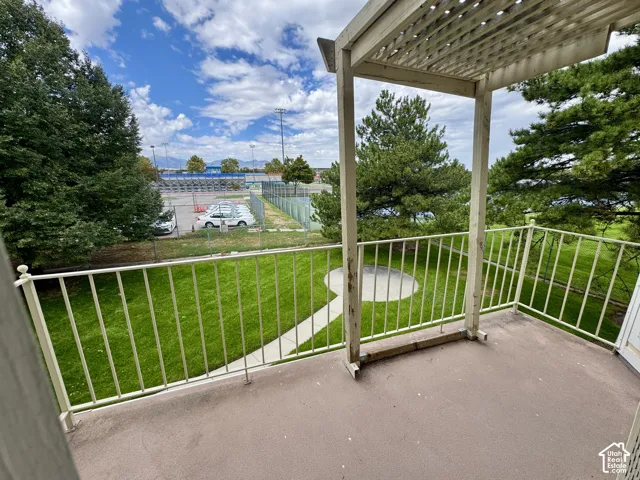 Private balcony with a slatted pergola, overlooking a landscaped lawn with a circular patio, and mature trees