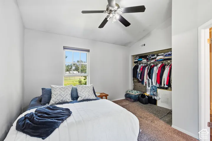 Vaulted ceiling with a ceiling fan, window with exterior views, and an open closet