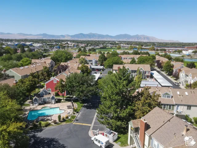 Community with multiple residential buildings, mature trees, a swimming pool, and mountain scenery in the background