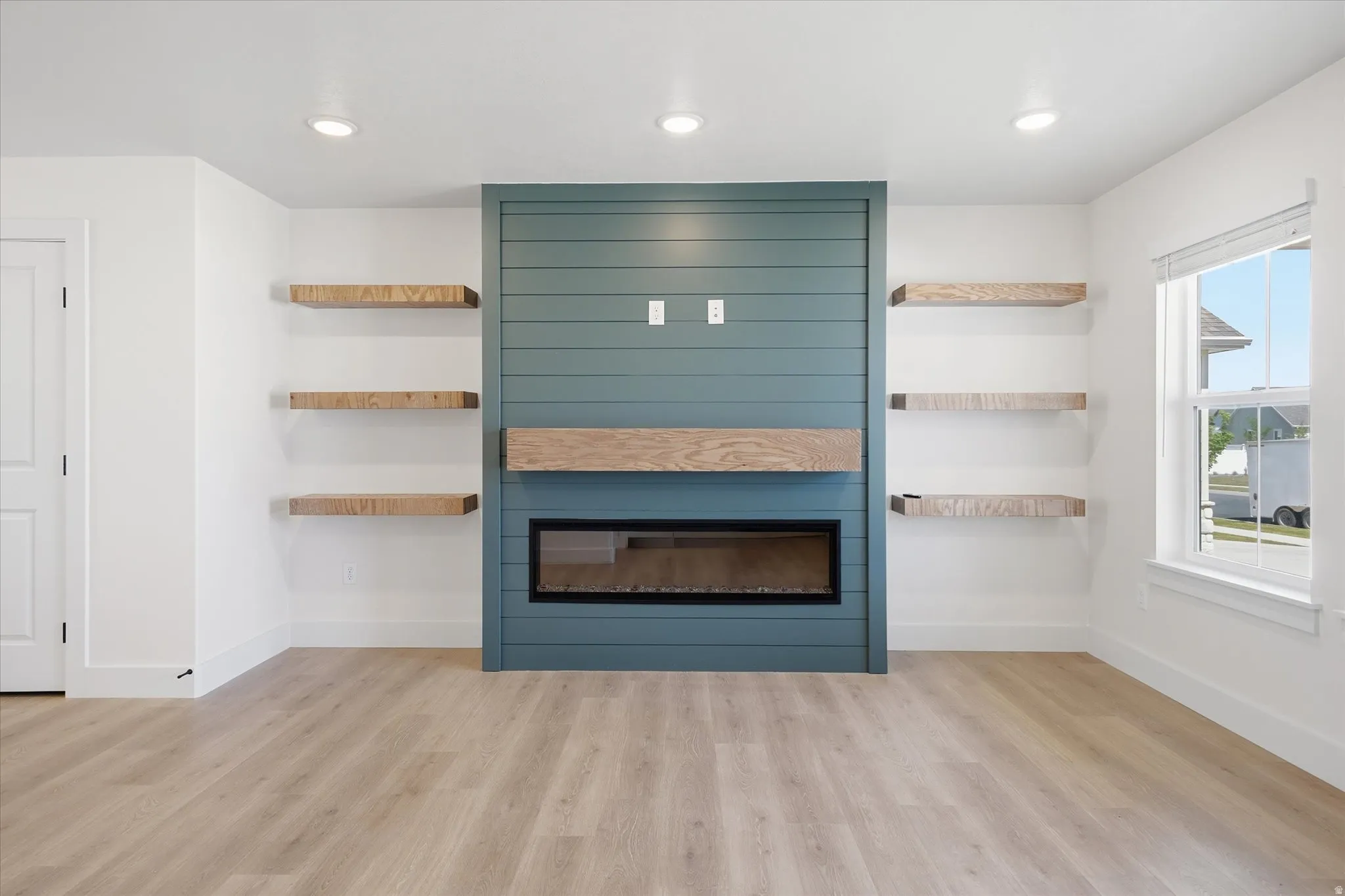 Recessed lighting, wood-finish flooring, linear electric fireplace, wood mantel, built-in shelving, and shiplap accent wall
