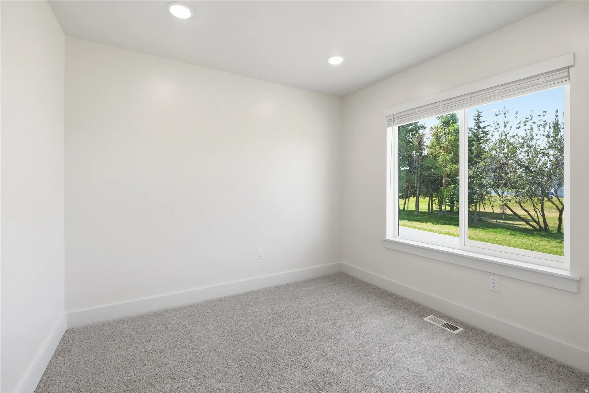 Recessed lighting, light gray carpeting, and a large window with white trim