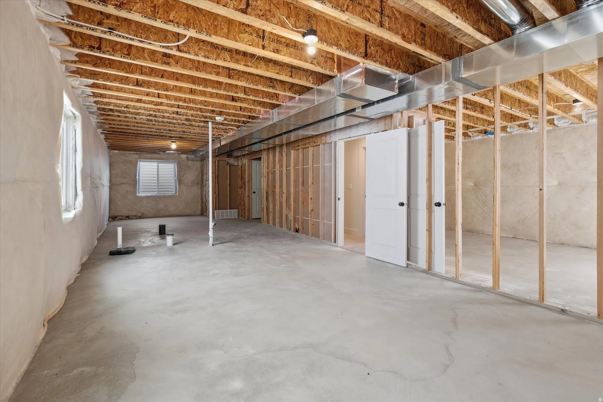 Unfinished basement with concrete flooring, exposed wood ceiling joists, and framed interior walls