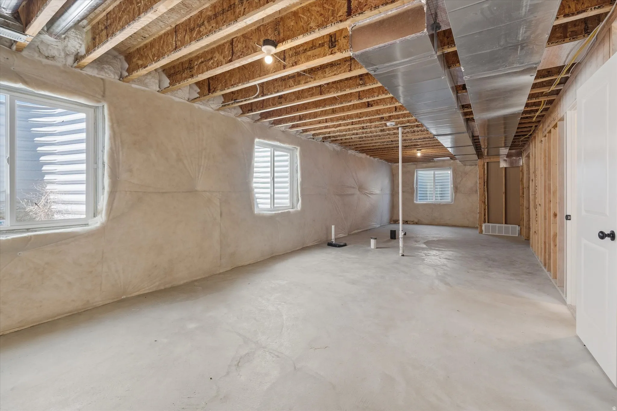 Unfinished basement with exposed wood joists, concrete flooring, multiple windows, and framed partition walls