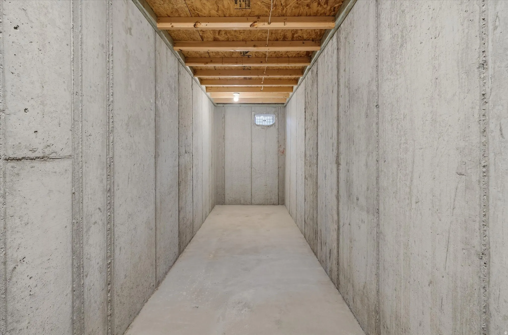 Unfinished basement with concrete slab flooring, concrete walls, and exposed wood joists