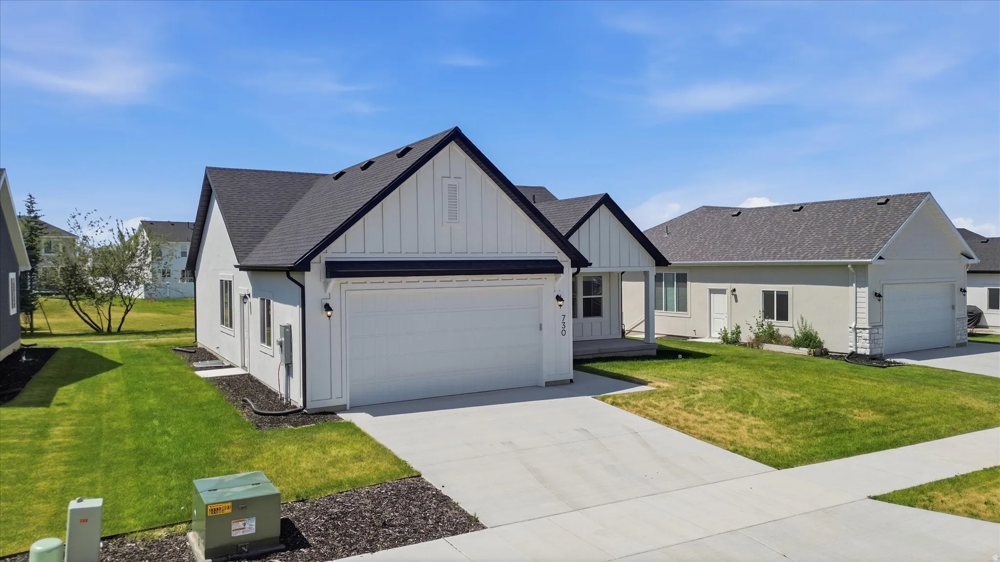 Contemporary residence featuring a white board and batten facade, dark shingle roof, attached garage with white door, concrete driveway, and front porch with dark columns