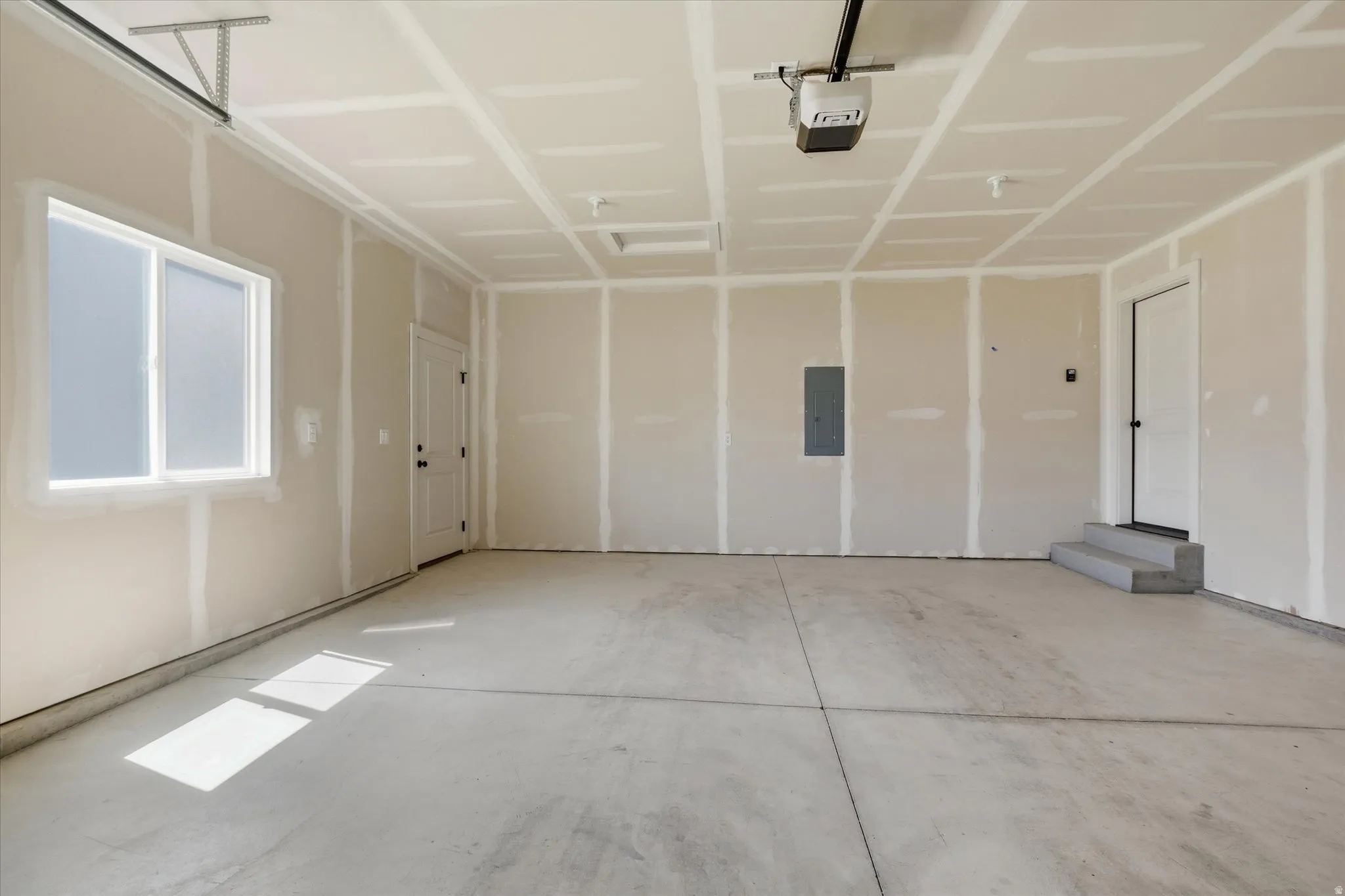 Spacious garage featuring a concrete floor, window, interior door, and garage door opener