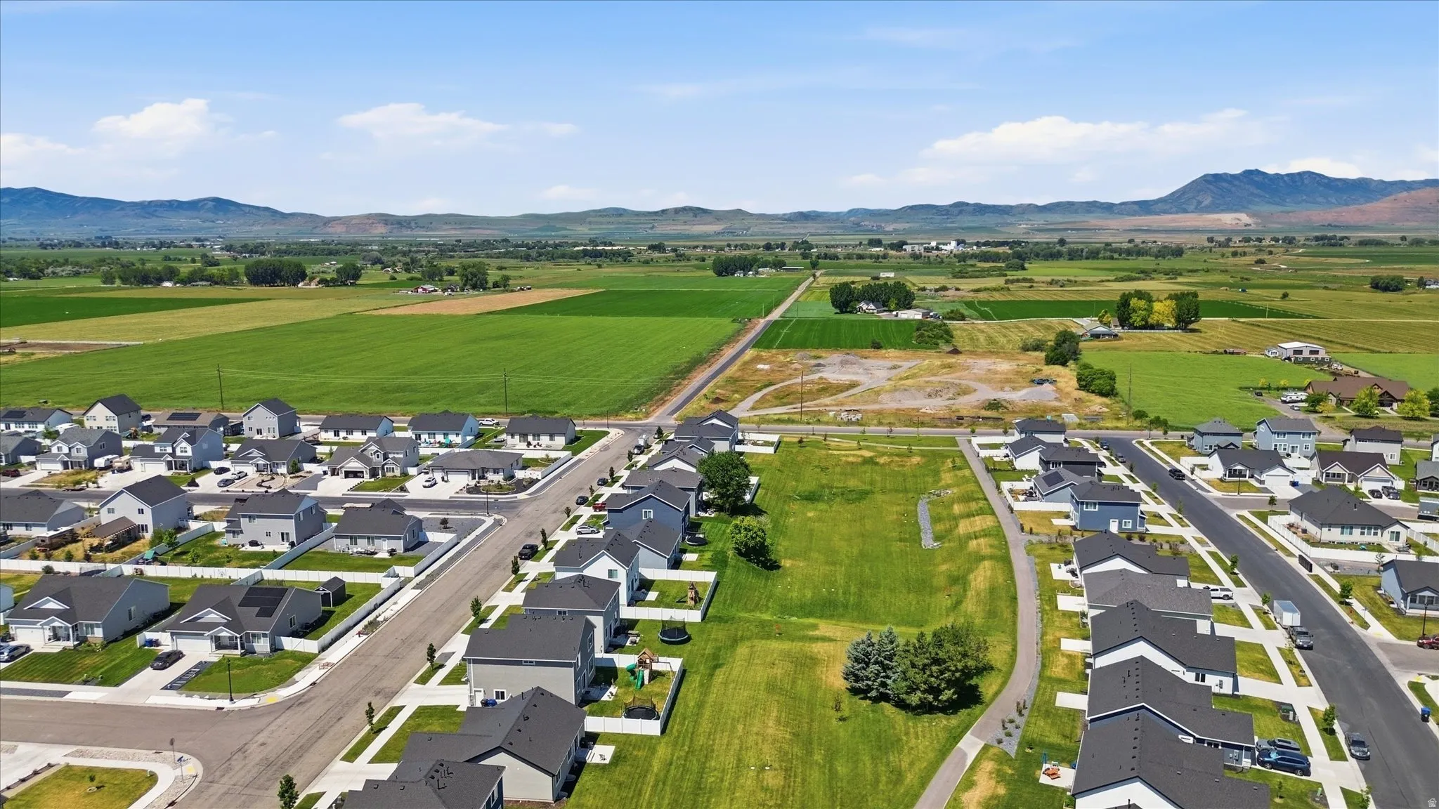 Residential development with paved roads and sidewalks, surrounded by agricultural fields and distant mountains