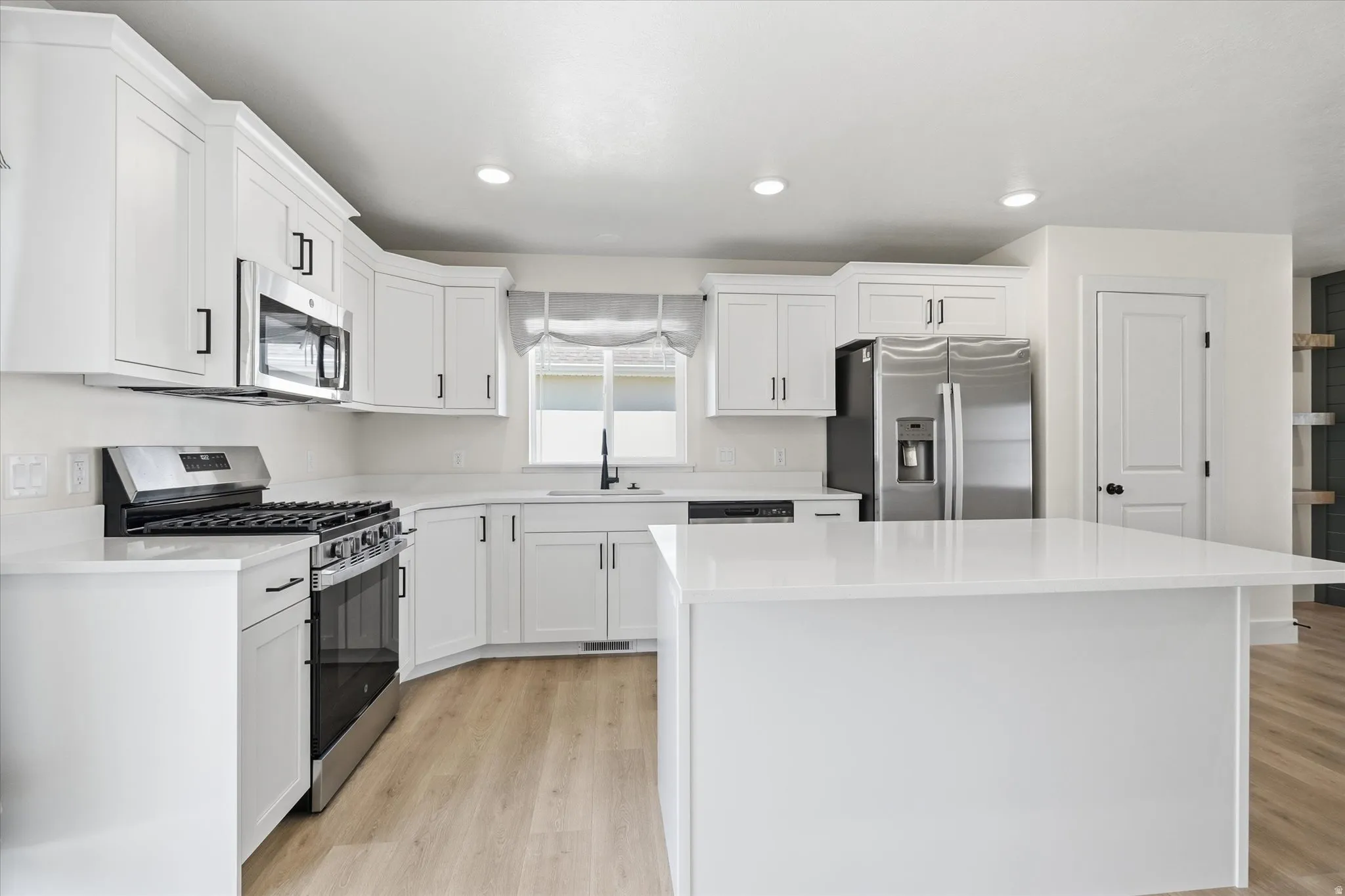 Kitchen featuring white cabinetry, stainless steel appliances, a center island, light wood-finish flooring, and recessed lighting