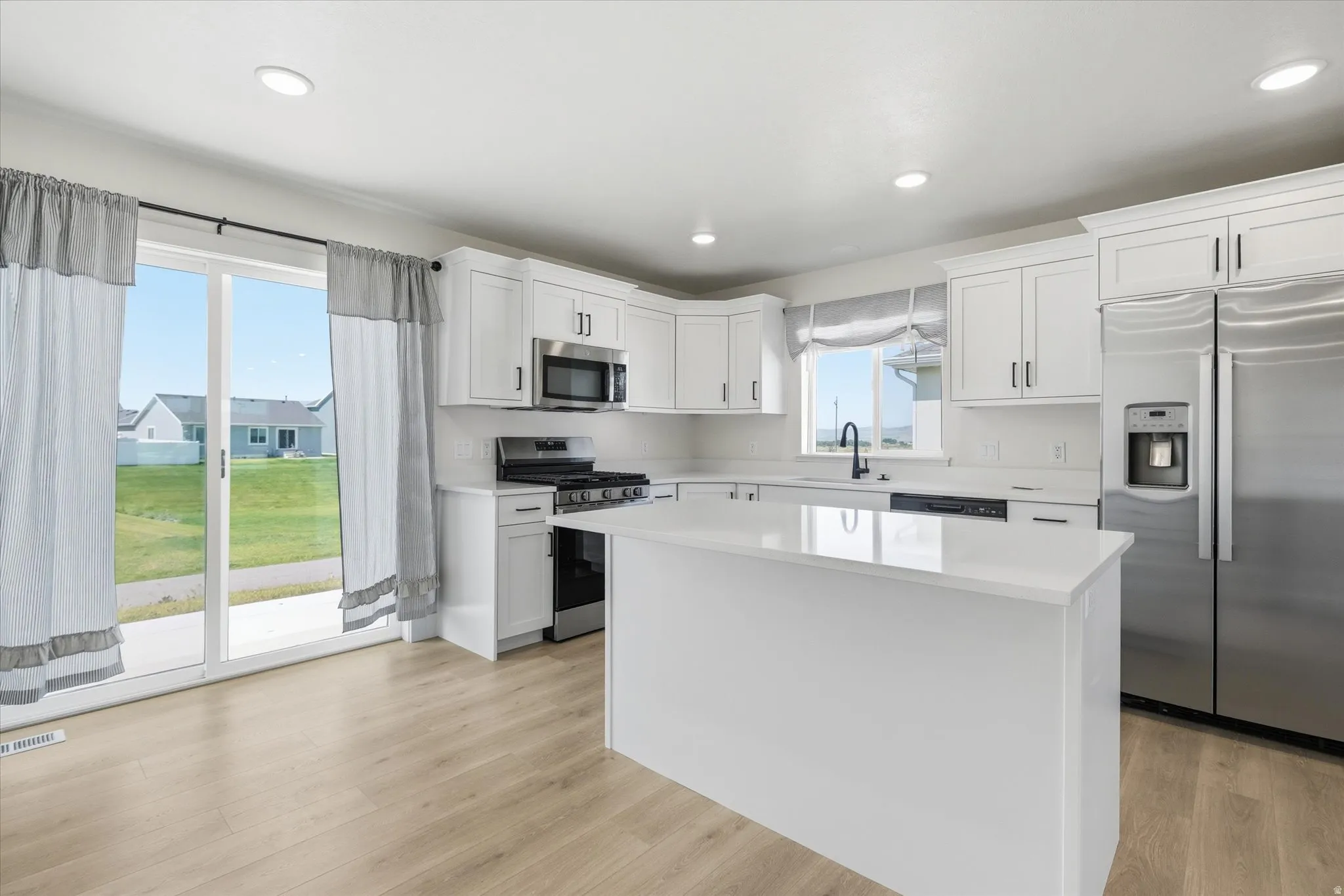 Modern kitchen with white cabinetry, stainless steel appliances, a center island with a solid surface countertop, and wood-finish flooring