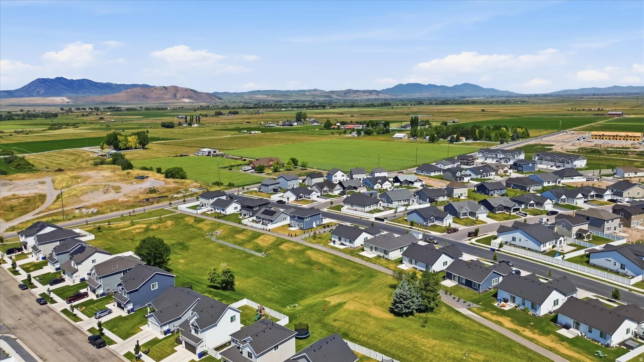 Expansive residential development featuring modern single-family homes, surrounded by agricultural fields and distant mountains