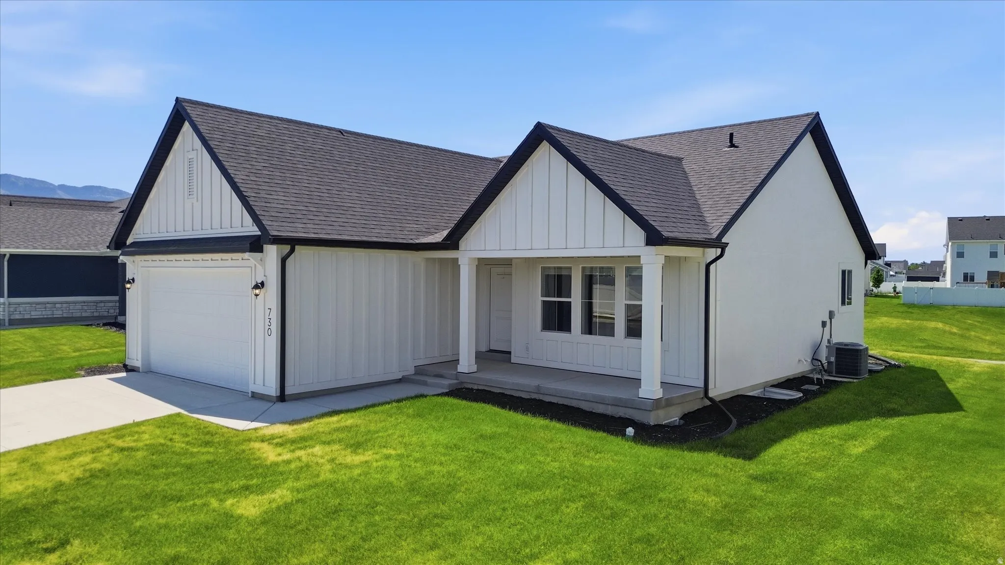 Contemporary ranch-style residence featuring a dark shingle roof, white vertical and horizontal siding, an attached garage with a concrete driveway, and a covered front porch with white columns