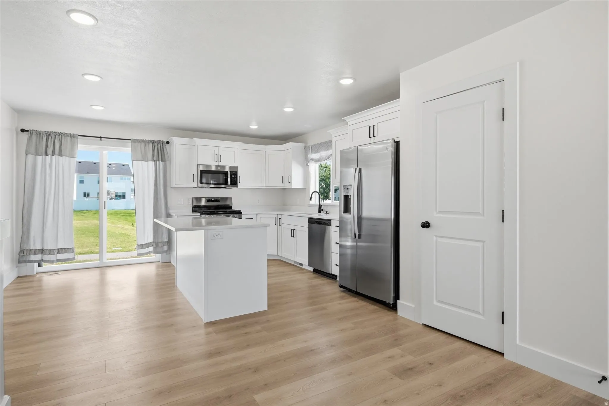 Kitchen featuring white cabinetry, stainless steel appliances, a center island with a light-toned countertop, and wood-finish flooring