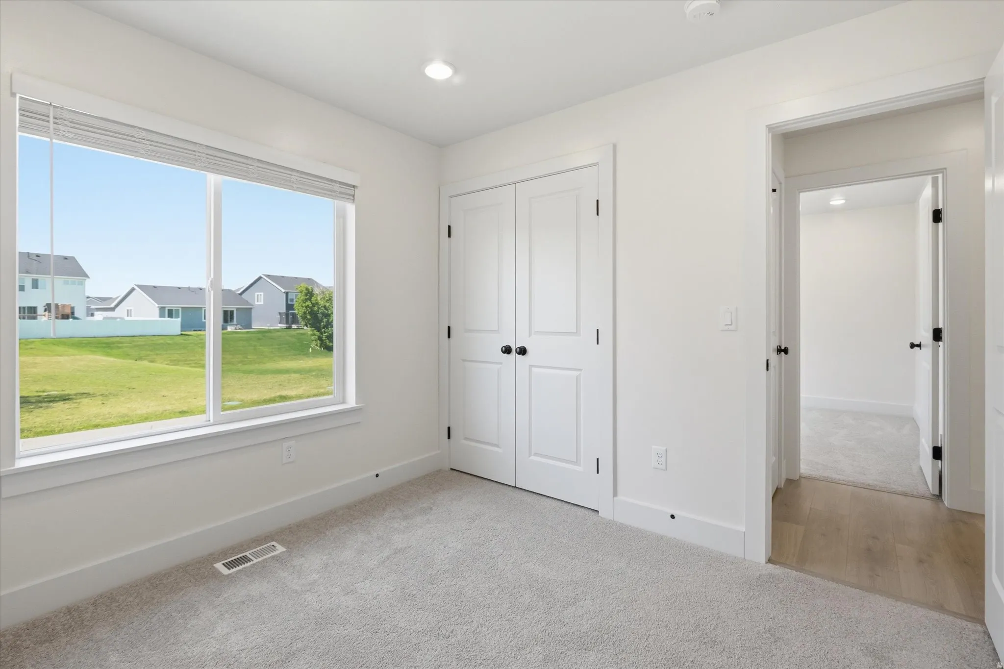 Recessed ceiling lighting, light gray carpeting, white double bi-fold closet doors, white trim, and a large window