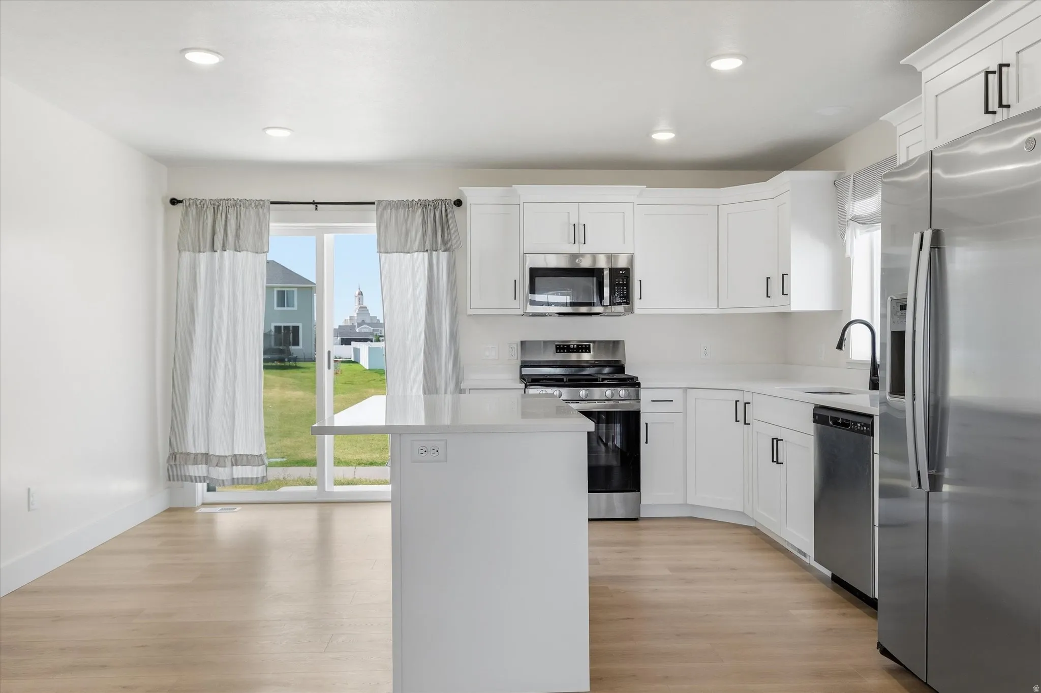 White cabinetry with black hardware, stainless steel appliances, light wood-finish flooring, recessed lighting, and a white countertop island