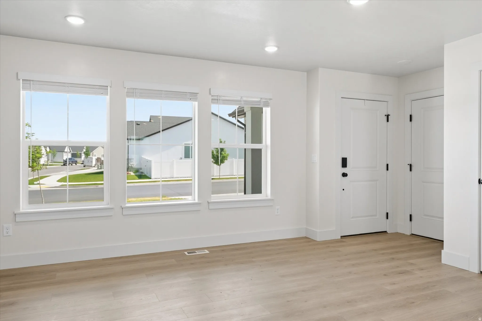 Spacious interior with three large windows, wood-finish flooring, recessed lighting, and white paneled doors