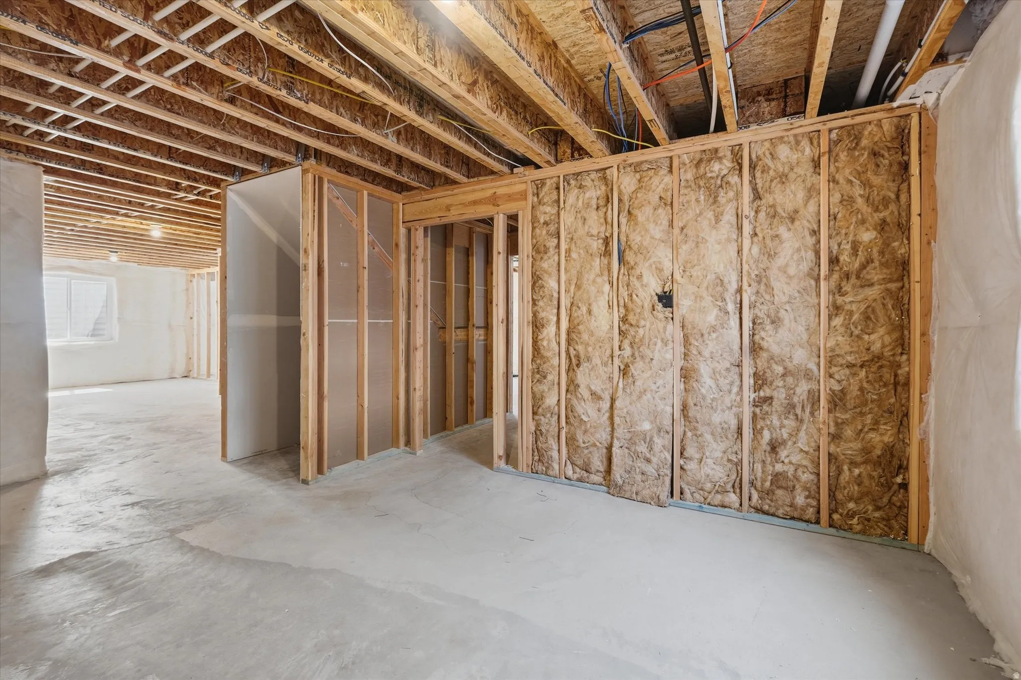 Unfinished basement offering exposed wood framing, concrete flooring, and partial wall insulation