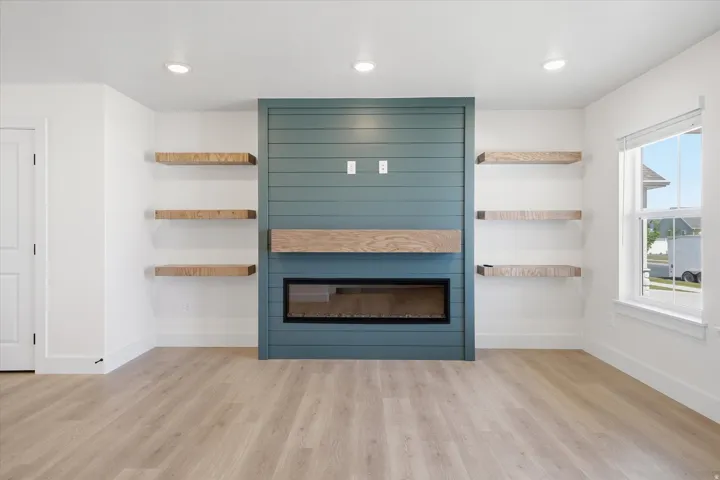 Recessed lighting, wood-finish flooring, linear electric fireplace, wood mantel, built-in shelving, and shiplap accent wall
