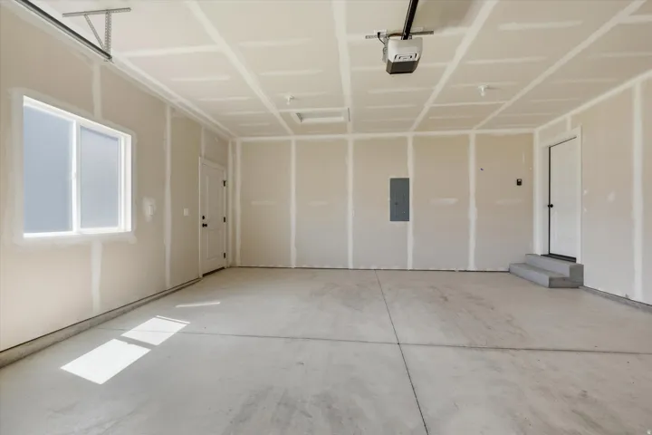 Spacious garage featuring a concrete floor, window, interior door, and garage door opener