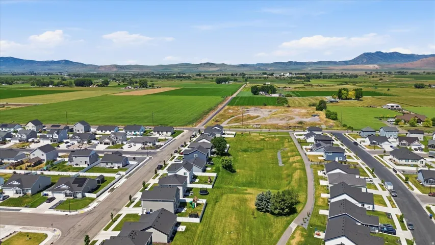 Residential development with paved roads and sidewalks, surrounded by agricultural fields and distant mountains