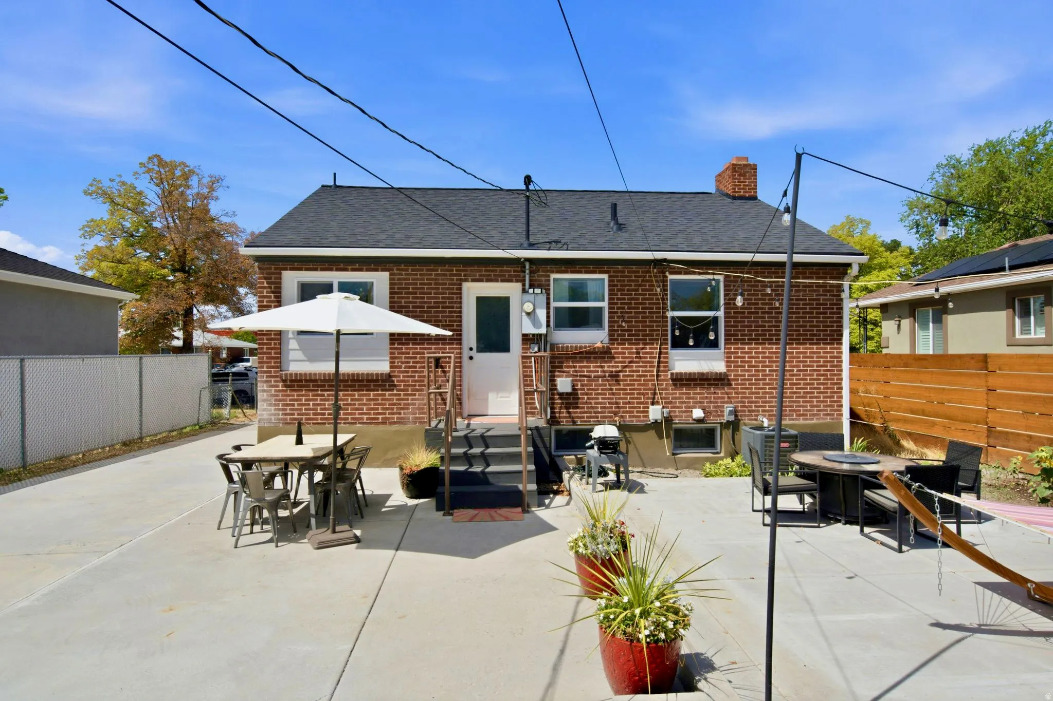 Brick exterior with a dark shingle roof, concrete patio, and a wood privacy fence