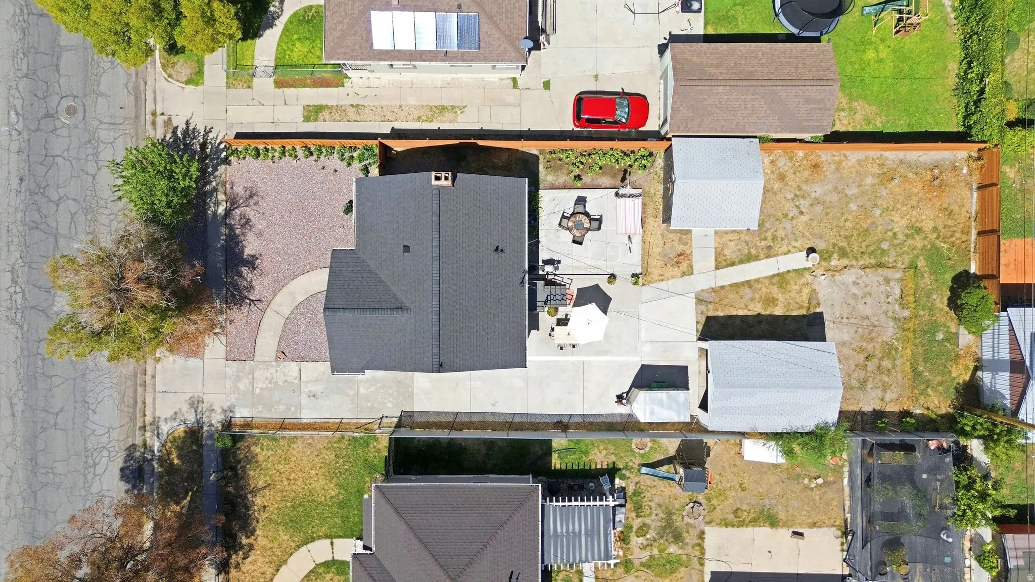 Expansive lot with a main residence, two detached outbuildings, a paved patio, and a gravel front yard with a curved walkway