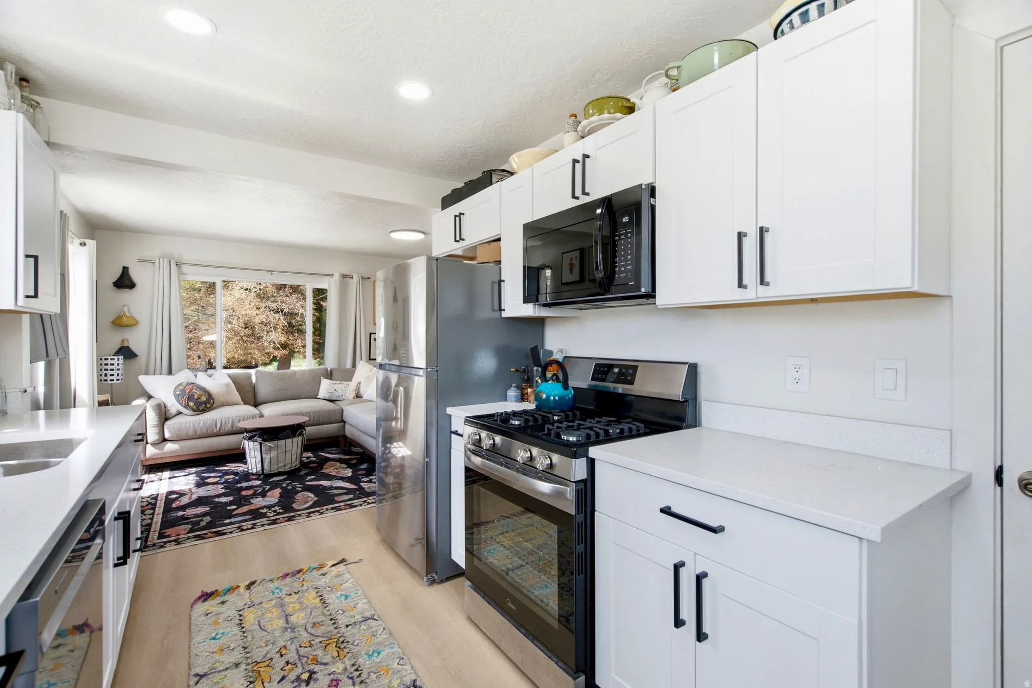 White shaker cabinetry, light countertops, stainless steel appliances, and wood-finish flooring