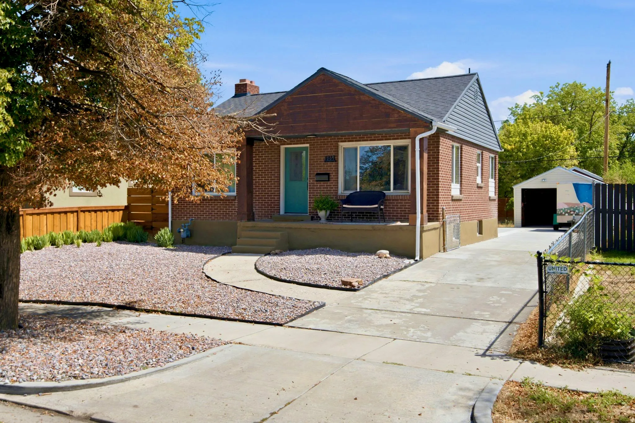 Brick exterior with a gabled roof and siding, featuring a covered porch, established trees, and a detached garage with a long driveway