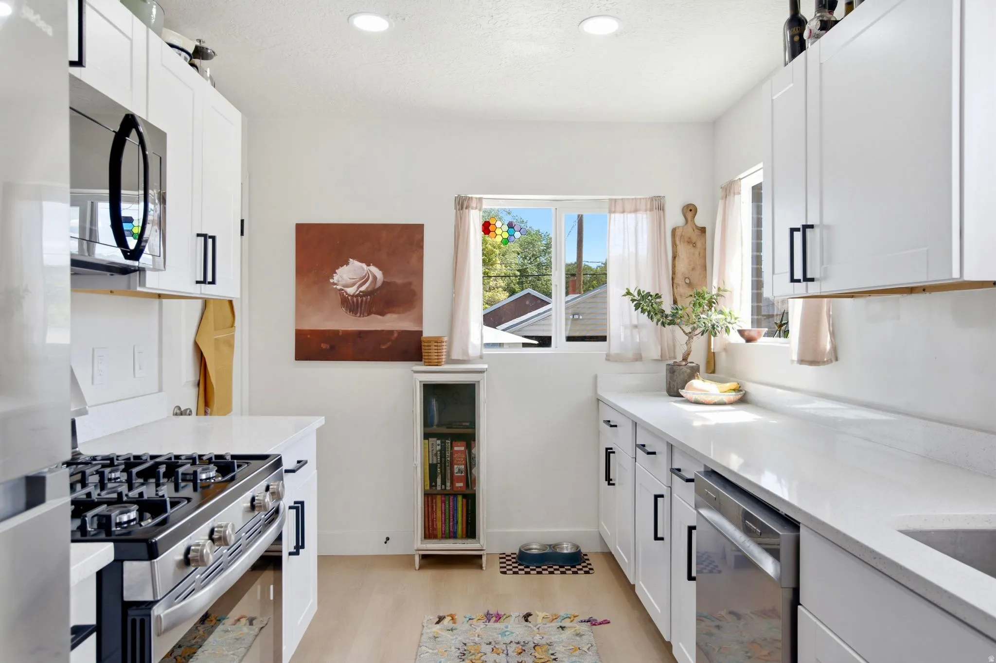 White cabinetry with black hardware, stainless steel appliances, light wood-finish flooring, recessed lighting, and a built-in oven range