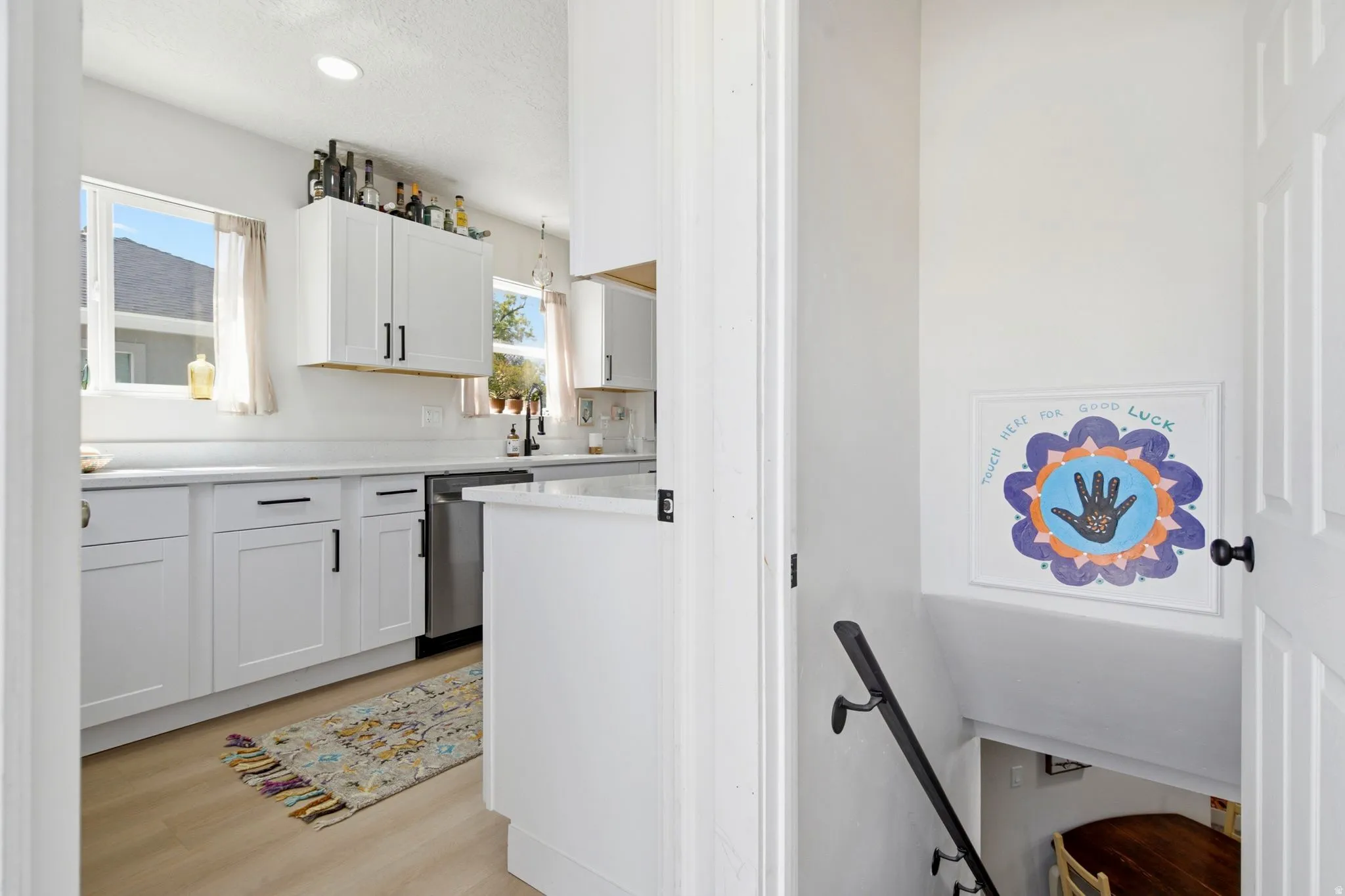 Kitchen featuring white cabinetry, light-toned countertops, a stainless steel dishwasher, and wood-finish flooring