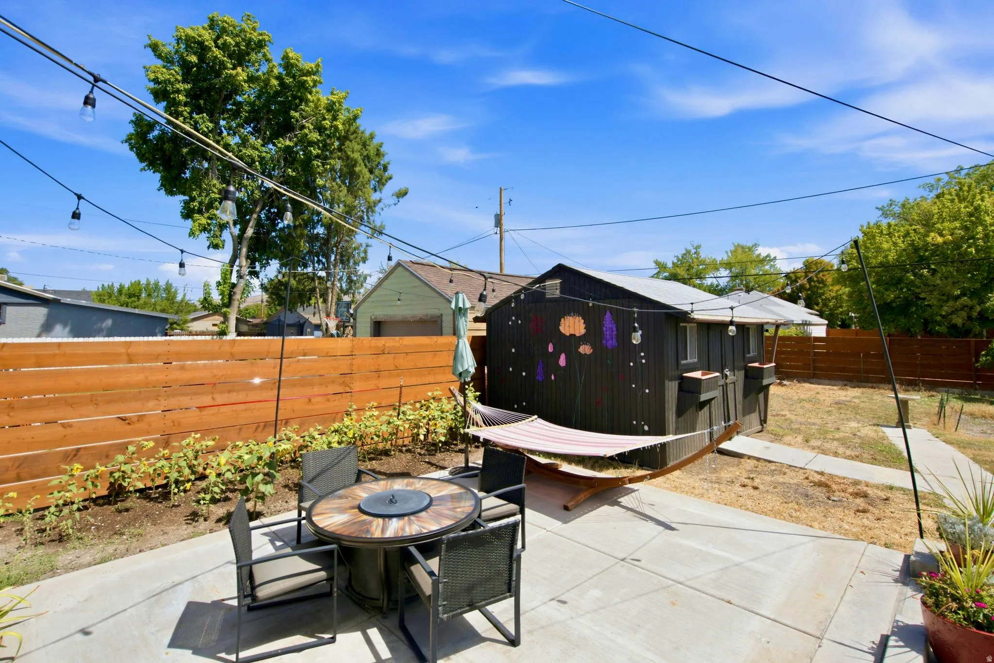 Concrete patio with string lighting, wood privacy fence, and a detached structure